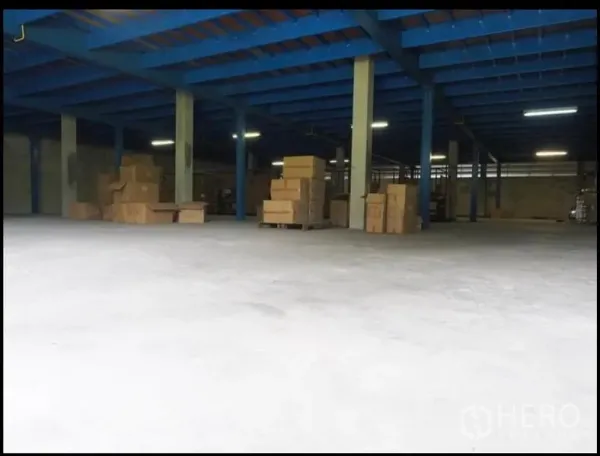 Warehouse for rent in Nakhon Pathom - Open-plan warehouse interior with blue steel beams, concrete floor, and pallets of boxes.
