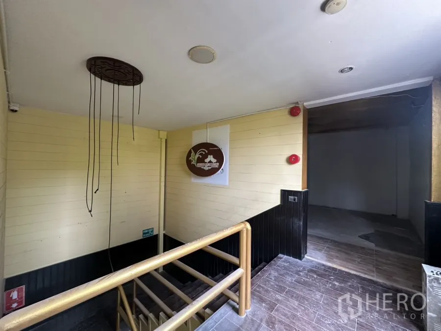 零售空间 出租在Bang Rak, Bangkok - 楼梯平台通往毛坯商铺楼层，带木质扶手与安全装置。