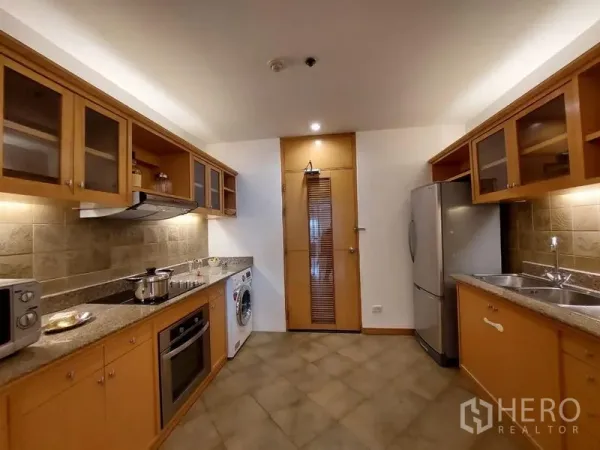 Apartment for rent - Closed kitchen with wood cabinetry, granite counters, tiled backsplash, fridge and washer in a Sathon apartment.