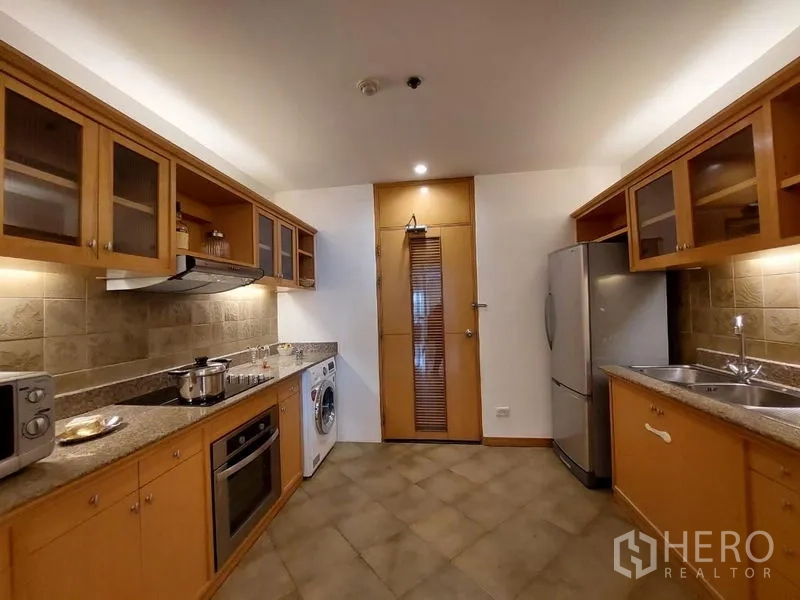 Apartment for rent - Closed kitchen with wood cabinetry, granite counters, tiled backsplash, fridge and washer in a Sathon apartment.