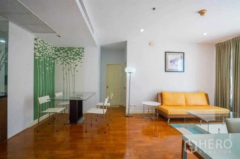 Condominium for rent or sale in Khlong Toei, Bangkok - Bright living and dining area with wood floors, glass table, and a yellow sofa.