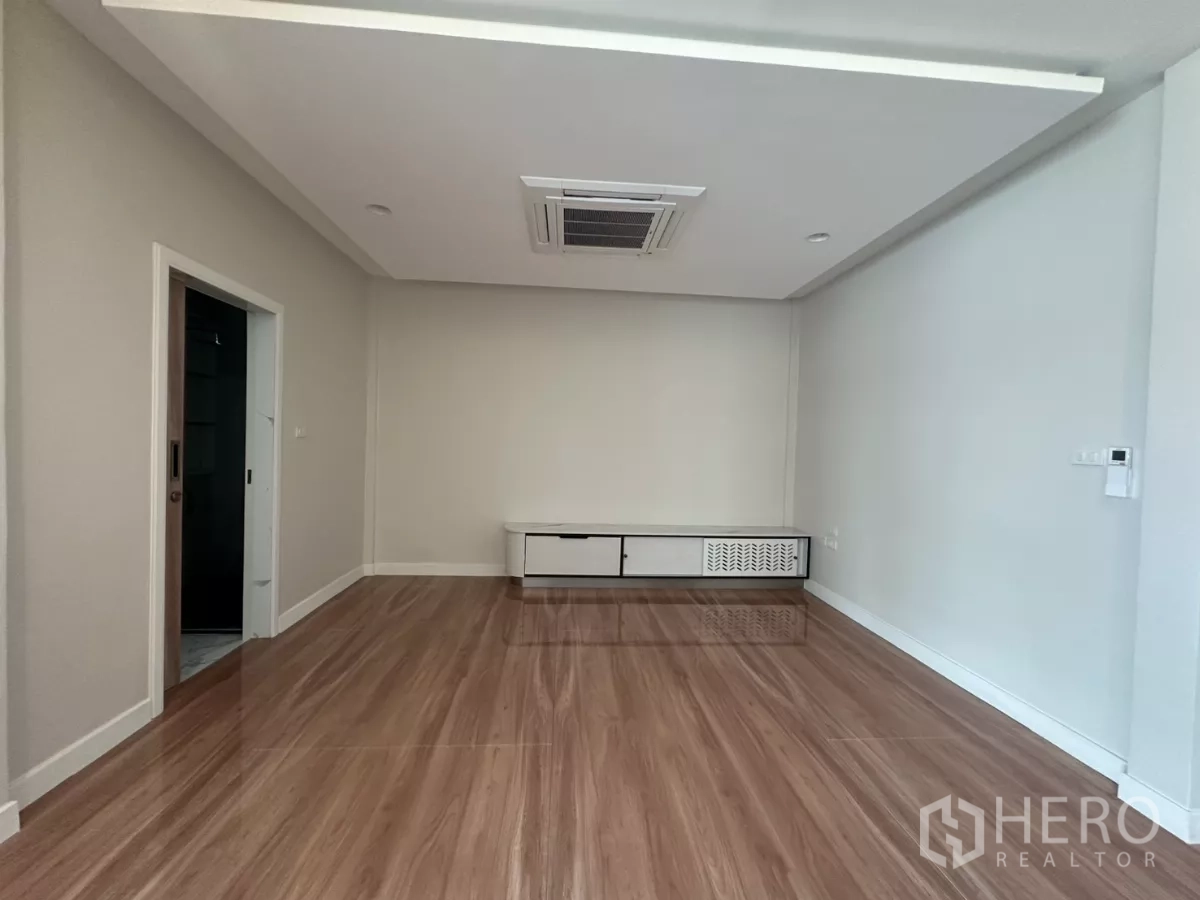 Townhouse for rent in Watthana, Bangkok - Empty room with glossy wood floors and a low TV cabinet.