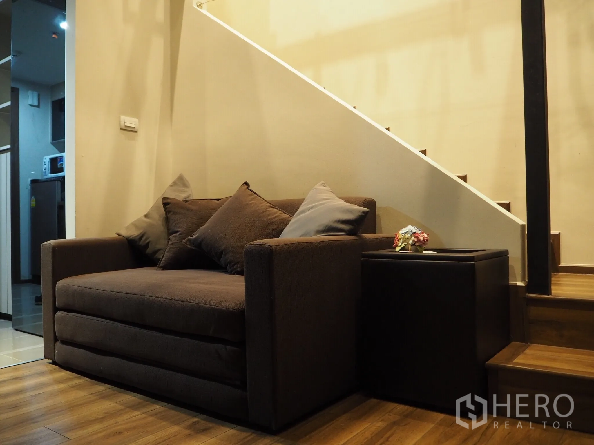 คอนโด ให้เช่าในPhaya Thai, Bangkok - มุมนั่งเล่นโซฟาสีน้ำตาลข้างบันไดไม้ ในคอนโดสไตล์ลอฟต์