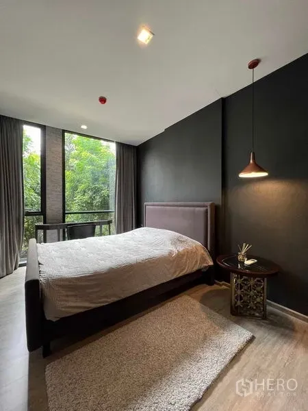 公寓 出租在Watthana, Bangkok - 卧室采用深色点缀墙与吊灯，落地窗外是葱郁绿景。