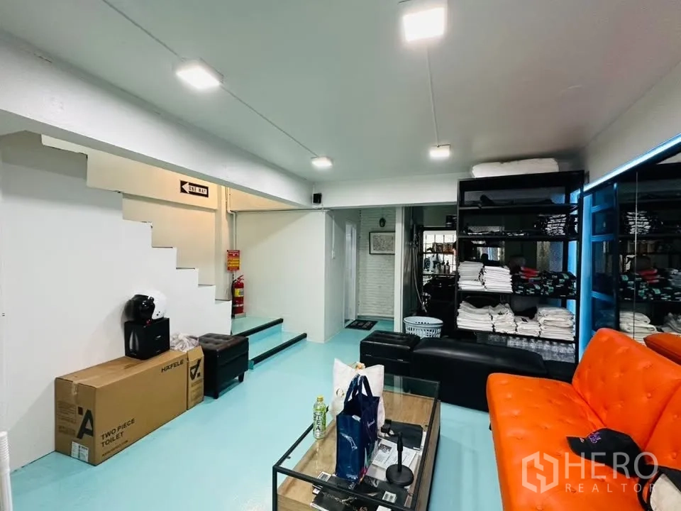 อาคารพาณิชย์ for sale in Watthana, Bangkok - โซนนั่งพักและเก็บของ โซฟาสีส้ม ชั้นวางของ และบันไดภายใน