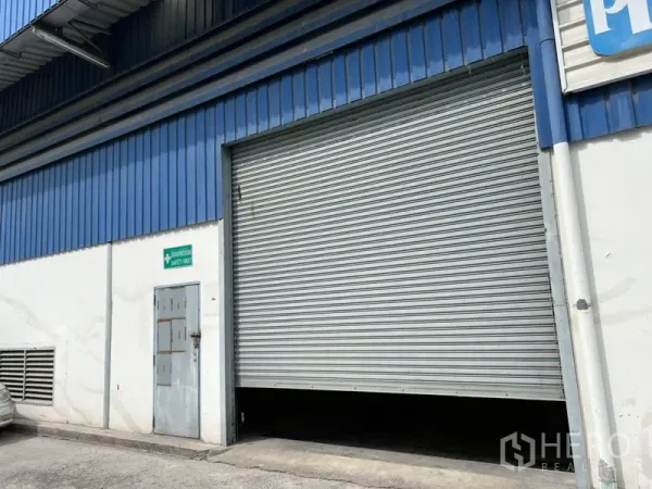 货栈 出租在Suan Luang, Bangkok - 仓库外观：大型金属卷闸装卸门与蓝色金属板外墙。