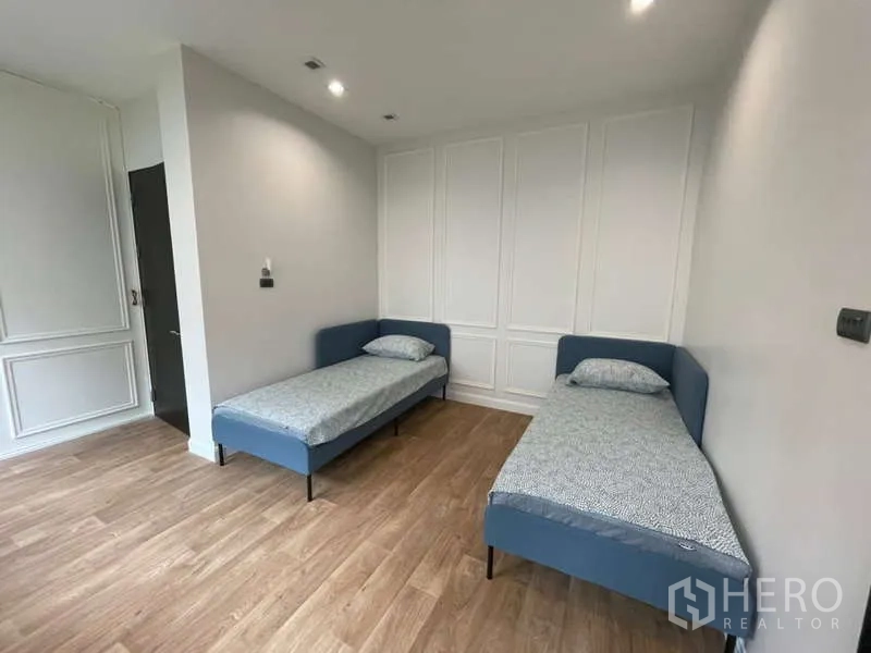 Detached House for rent or sale in Lat Krabang, Bangkok - Guest bedroom offering two single beds, paneled walls and wood-look flooring.