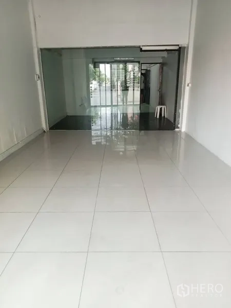 Shophouse for rent in Phra Khanong, Bangkok - Bright ground-floor retail space with glossy white tiles, high ceiling, and a glass partition leading to a sliding door.