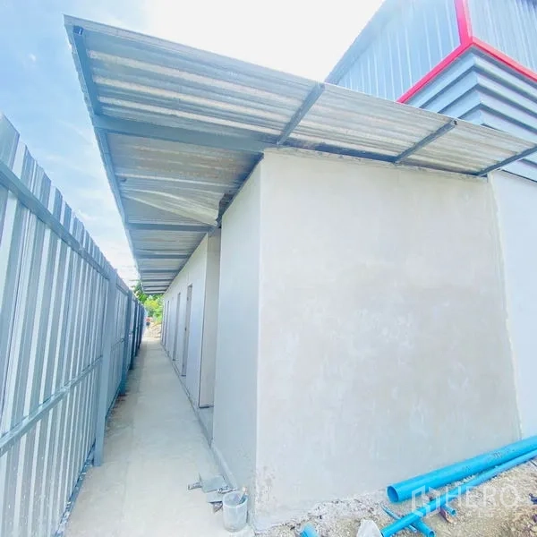 Warehouse for rent in Bang Khae, Bangkok - Side service block with lean‑to metal roof and walkway, plus visible blue utility pipes.