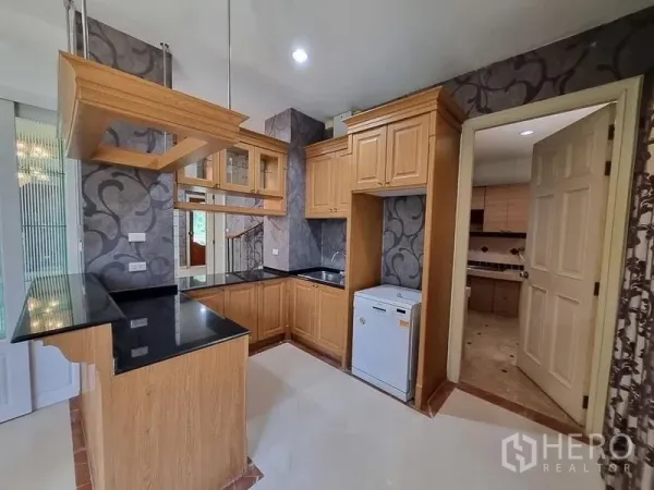 Detached House for rent in Yan Nawa, Bangkok - Pantry kitchen with wood cabinetry, black granite counters and doorway to a separate Thai kitchen.