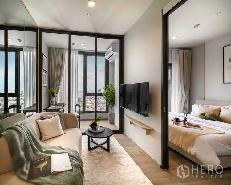 公寓 出租在Chatuchak, Bangkok - 采光充足的客厅，玻璃隔断与卧室相连，挂墙电视，通向观景阳台俯瞰城市。