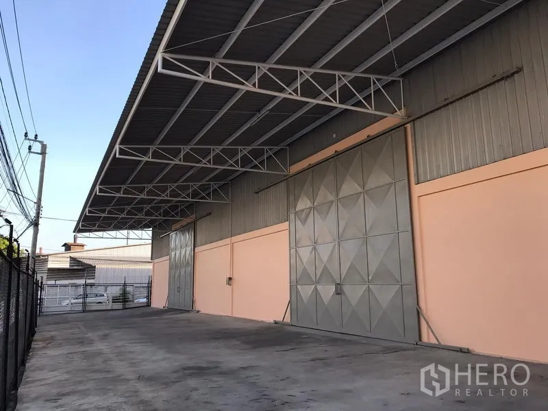 Factory for rent in Mueang Samut Prakan, Samut Prakan - Factory exterior showing covered loading bay, wide sliding steel doors and a secured driveway.