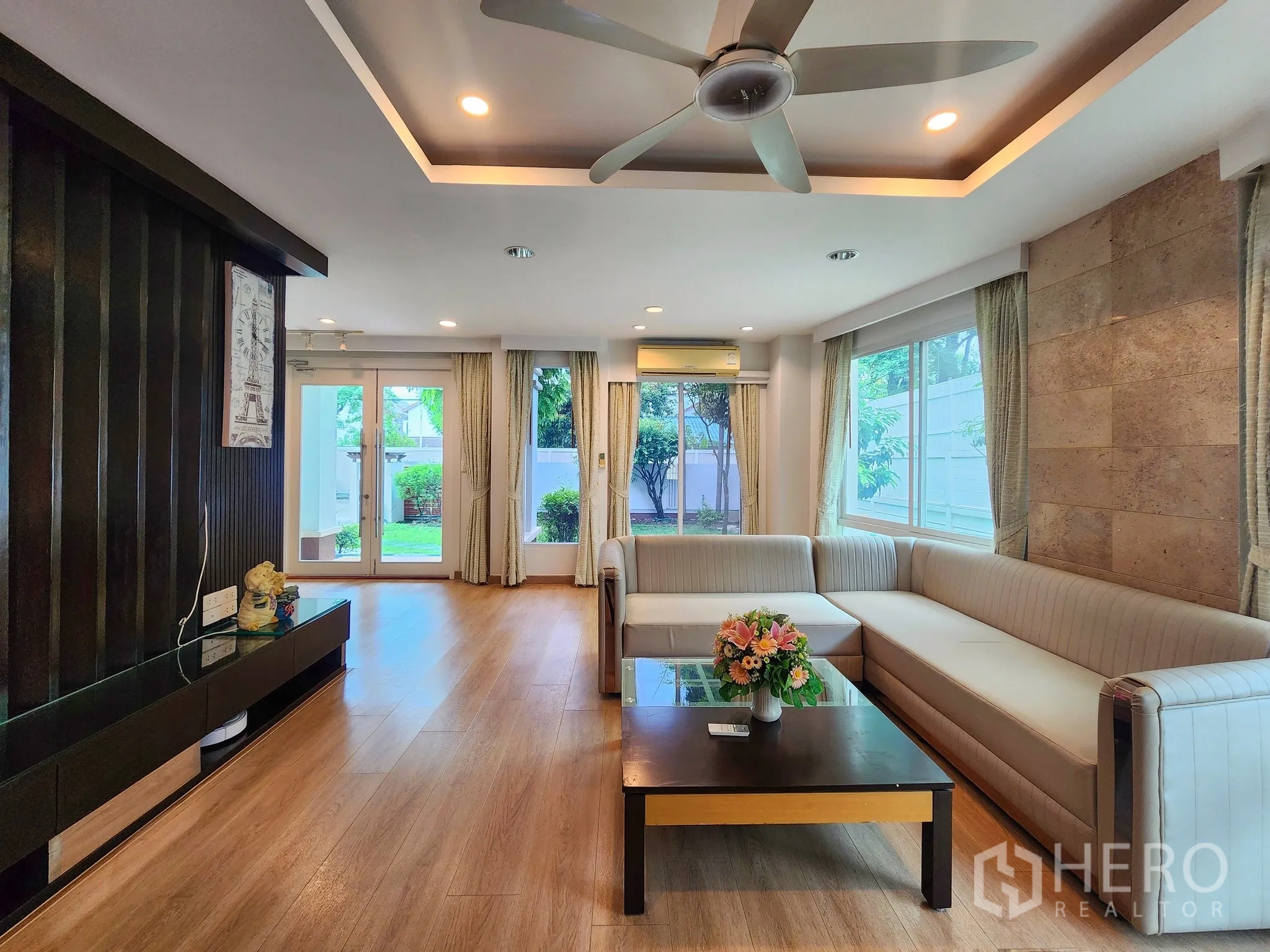 Detached House for rent in Bang Kapi, Bangkok - Open living area featuring sectional sofa, media wall and large windows.