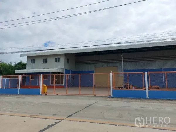 Factory for rent in Lat Lum Kaeo, Pathum Thani - Gated factory exterior with blue-and-orange fence and wide loading entrance.