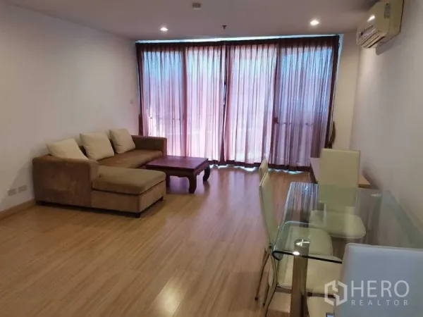 公寓 出租在Khlong Toei, Bangkok - 明亮客餐厅，转角沙发与玻璃餐桌，木地板，整面落地窗与窗帘。