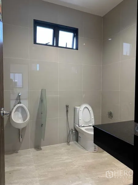 Factory for rent or sale in Lam Luk Ka, Pathum Thani - Restroom with toilet, urinal, window and black countertop vanity.