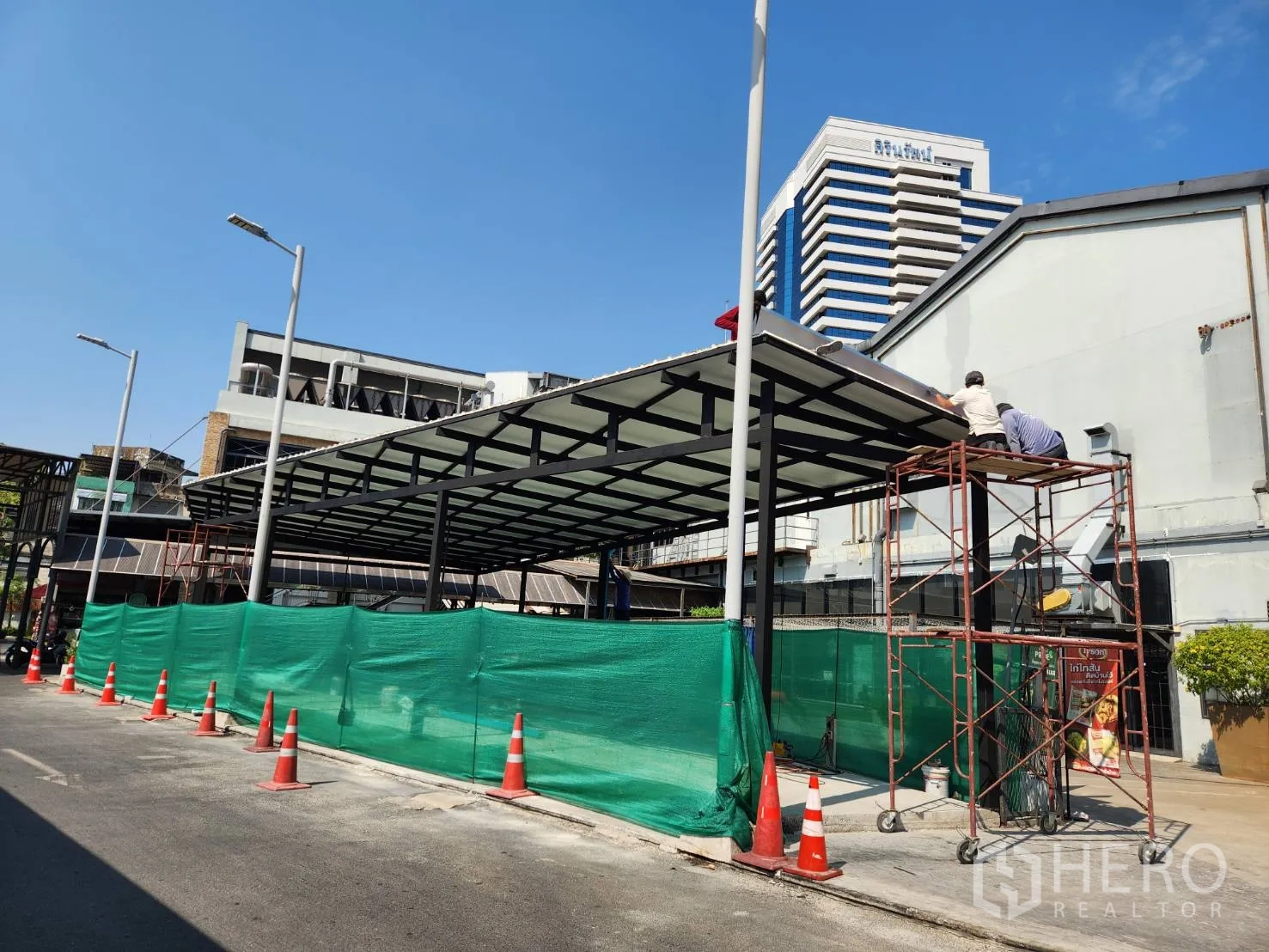 零售空间 出租在Khlong Toei, Bangkok - 道路侧视图，钢结构雨棚商铺配脚手架与绿色围挡，位于曼谷商务区。