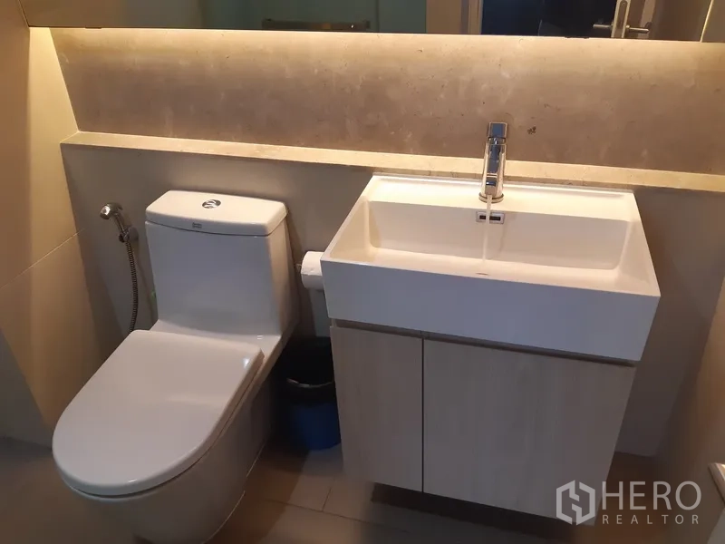 Condominium for rent in Khlong Toei, Bangkok - Contemporary bathroom with vanity sink cabinet and toilet in soft lighting.