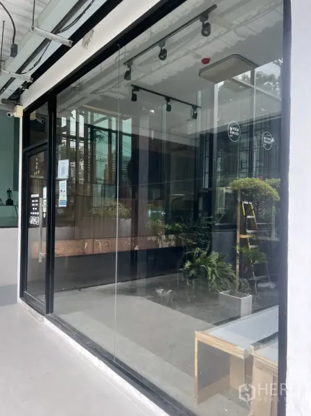 零售空间 出租在Watthana, Bangkok - 临街零售铺面，整面落地玻璃门窗，黑色金属框架，内有轨道灯与水泥地面