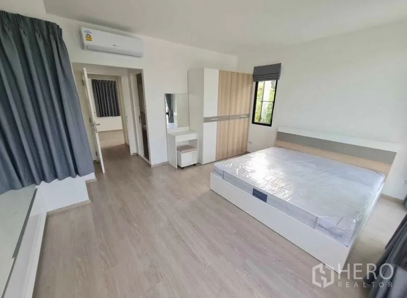 Townhouse for rent in Bang Phli, Samut Prakan - Second angle of airy bedroom with bed, wardrobe, mirror and AC over light wood floor.