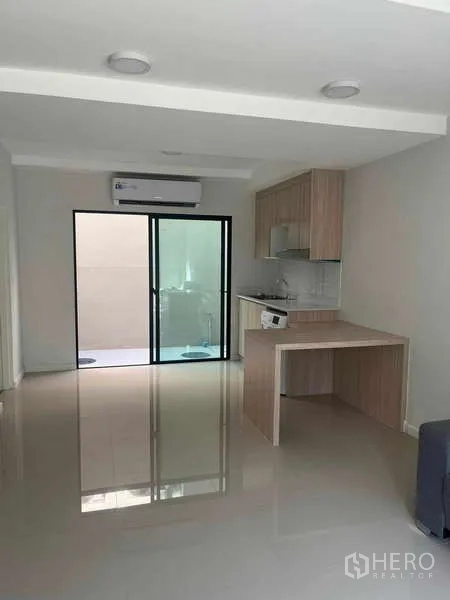 Townhouse for rent in Suan Luang, Bangkok - Open-plan living area with glossy floors, sliding glass doors and a kitchen at the back.