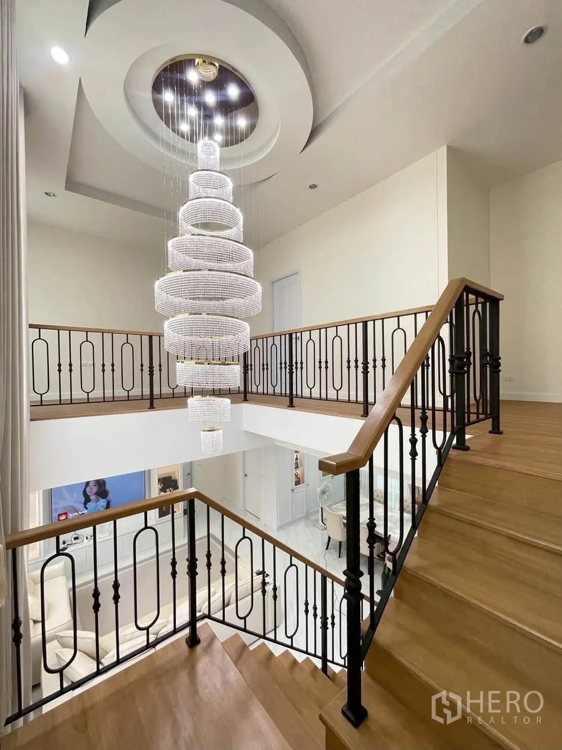 Detached House for rent or sale in Bang Phli, Samut Prakan - Staircase with wooden steps and wrought-iron balustrade beneath a dramatic multi-tier chandelier.