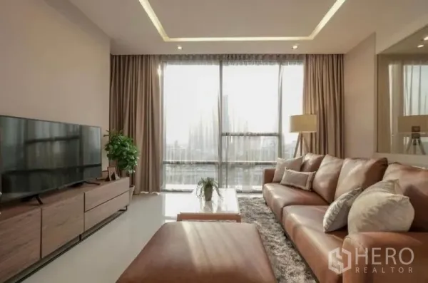 Condominium for rent in Sathon, Bangkok - Sunlit living room with floor-to-ceiling windows, leather sectional sofa, TV console and city view.