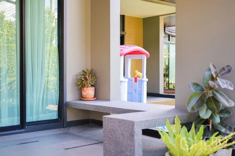 Detached House for rent or sale in Lam Luk Ka, Pathum Thani - Shaded front patio with built-in bench, potted plants and sliding glass doors.