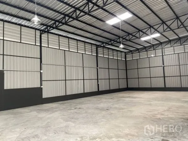 Warehouse for rent in Wang Thonglang, Bangkok - Open-plan storage hall with corrugated metal walls, hanging industrial lights, and tall clear-span ceiling.