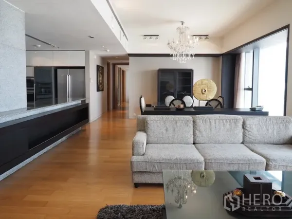 Condominium for rent in Sathon, Bangkok - Spacious lounge with gray sofa, dining set and built-in media wall beside large windows.