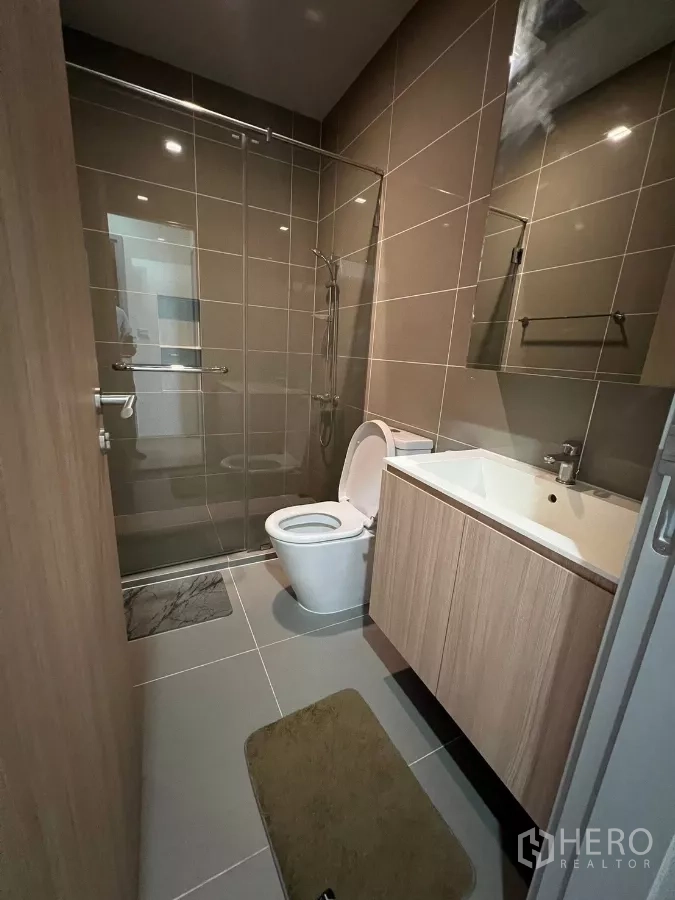 Condominium for rent or sale in Chatuchak, Bangkok - Bathroom with glass‑enclosed shower, vanity and toilet in neutral tiles.