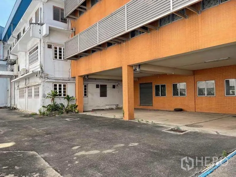 Factory for rent in Phra Samut Chedi, Samut Prakan - Covered loading bay with orange‑tiled facade, roller shutter door and open yard.