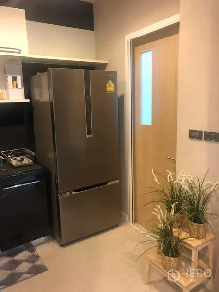 Detached House for rent or sale in Bang Kapi, Bangkok - Compact kitchen corner with a stainless refrigerator and a door, accented by plants.