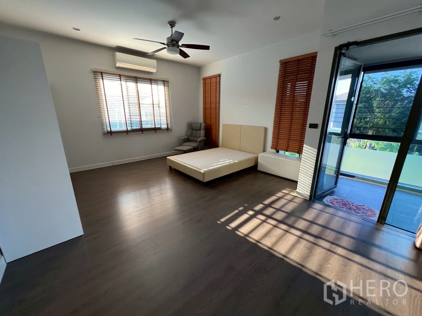 Detached House for rent in Bang Kapi, Bangkok - Spacious master bedroom with platform bed, armchair, and access to glassed balcony.