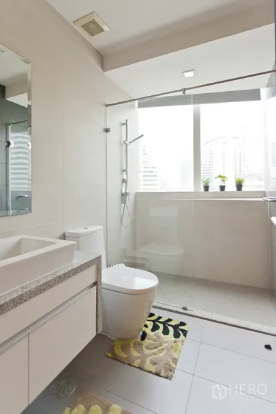 Condominium for rent in Khlong Toei, Bangkok - Contemporary bathroom with glass-enclosed shower, window light, and vanity.