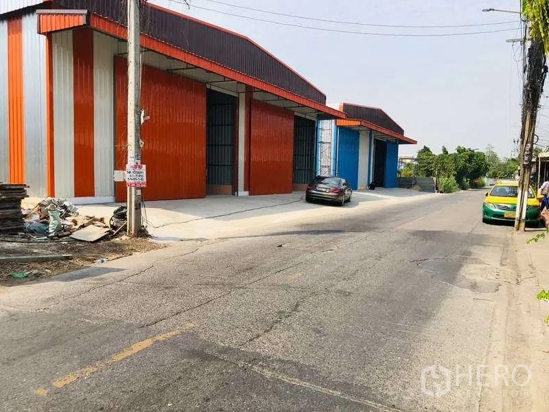 Warehouse for rent in Bueng Kum, Bangkok - Street-side view of colorful steel-clad warehouse units with wide loading aprons and parked cars in Bueng Kum.