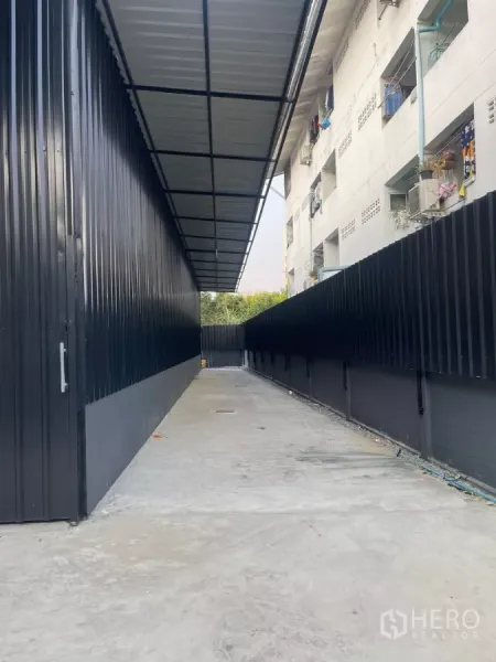คลังสินค้า ให้เช่าในWang Thonglang, Bangkok - ทางรถวิ่งคอนกรีตมีหลังคา ข้างอาคารโกดังผนังเมทัลชีทสีดำพร้อมรั้วทึบ