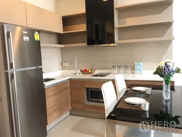 公寓 出租在Khlong Toei, Bangkok - L形厨房，木纹橱柜、不锈钢冰箱、电磁炉与两人餐台。