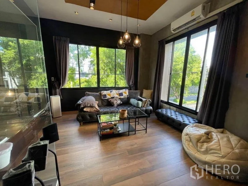 Townhouse for sale in Bang Phli, Samut Prakan - Bright lounge with large windows, greenery views, leather sofa and wood floors.