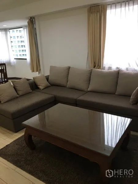 公寓 出租在Watthana, Bangkok - 带抱枕的L型沙发与木质茶几，窗边采光充足