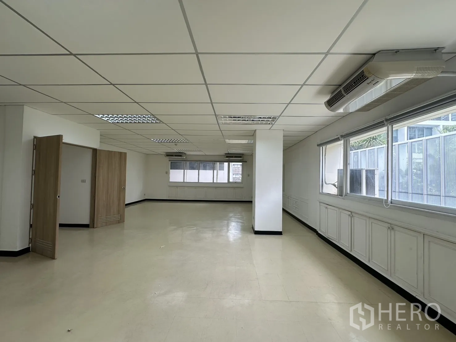 Office Space for rent in Pathum Wan, Bangkok - Long open workspace with large windows, a central column, ceiling air conditioners, and white paneling.