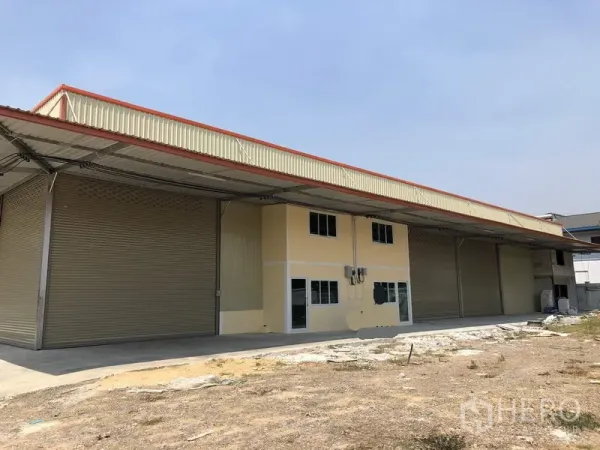 Factory for rent in Khlong Luang, Pathum Thani - Wide view of the factory facade showing multiple roller shutter doors and a concrete yard.
