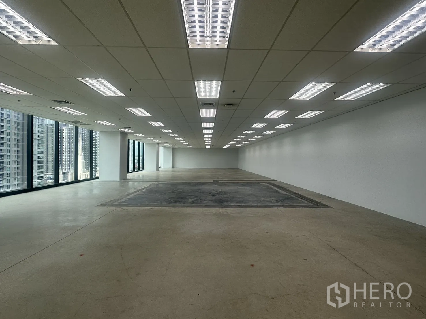ออฟฟิศ for rent in Ratchathewi, Bangkok - โถงสำนักงานยาวรูปทรงสี่เหลี่ยม พร้อมไฟฟลูออเรสเซนต์หลายแถวและผนังกระจกตลอดแนว