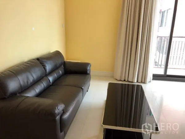 Condominium for rent or sale in Khlong Toei, Bangkok - Bright living room with black leather sofa, glossy tile floor, and curtain-lined balcony door.