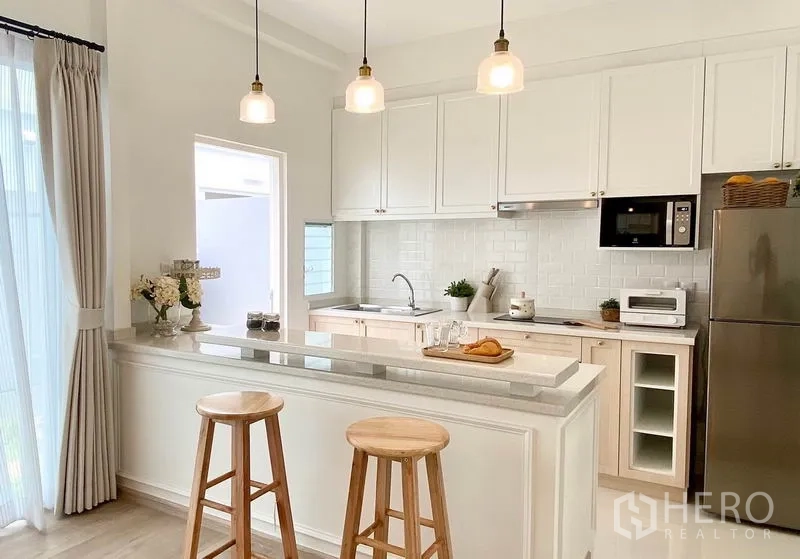 Townhouse for rent in Prawet, Bangkok - Close-up of the kitchen island with pendant lights, bar stools and white cabinetry.