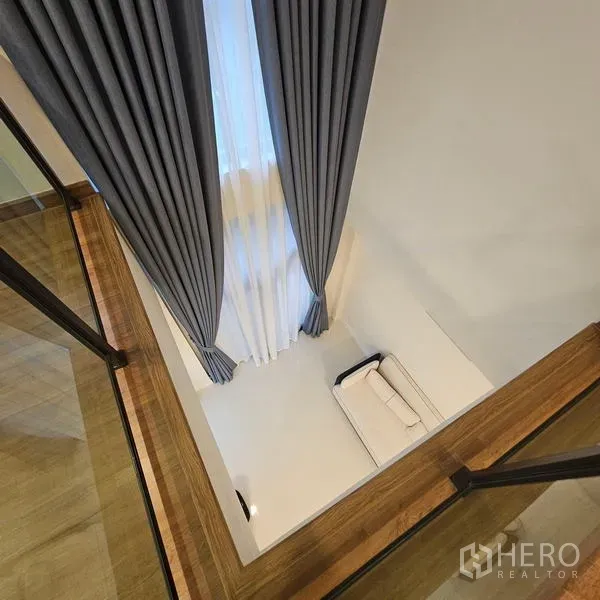 Detached House for rent in Saphan Sung, Bangkok - View from the upper floor into the double-height living area with floor-to-ceiling curtains and a sofa.
