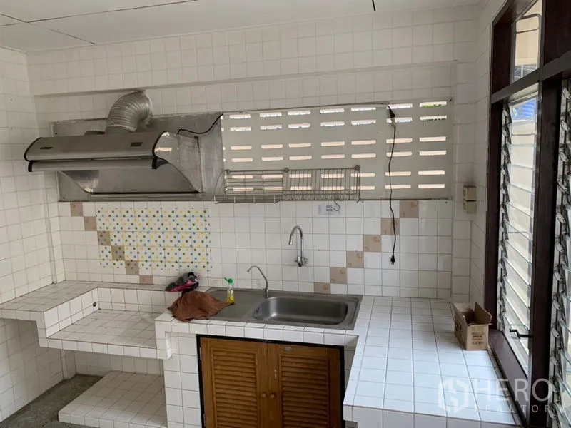 Townhouse for rent in Watthana, Bangkok - Thai kitchen with tiled counters, sink, range hood and louvered windows.