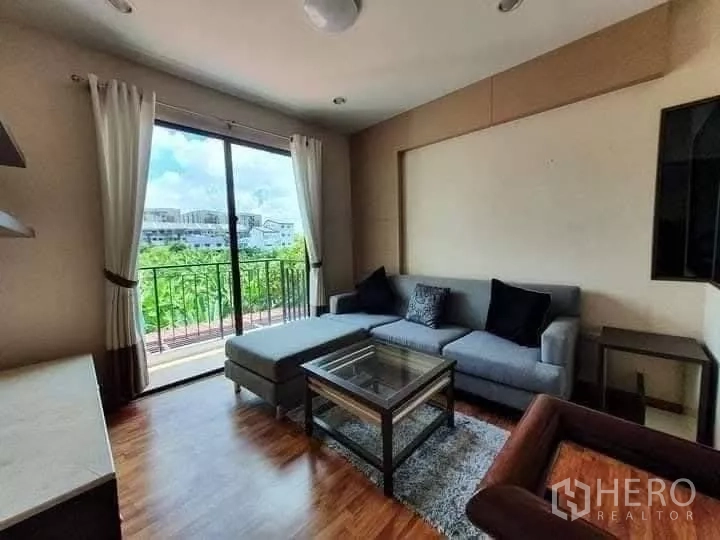 Townhouse for rent in Khlong Toei, Bangkok - Upper living room opening to a balcony with sectional sofa, glass table and leafy outlook.