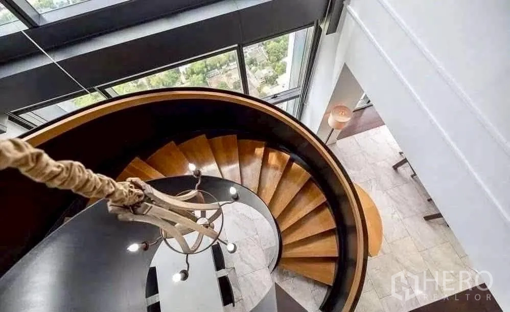 Condominium for rent in Sathon, Bangkok - Elegant curved staircase viewed from above beside tall windows.