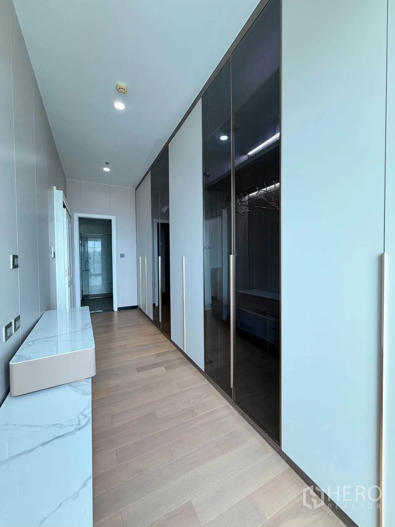 Condominium for sale in Watthana, Bangkok - Hallway with glass-front wardrobes and long console over wood flooring.